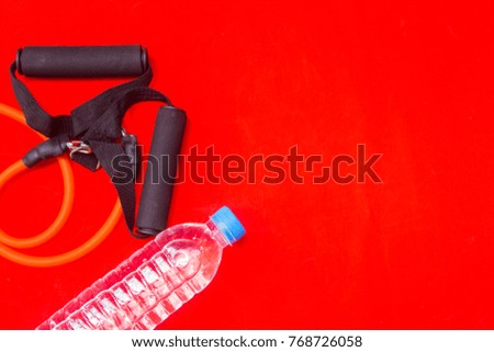 Resistance band and plastic water bottle on red background