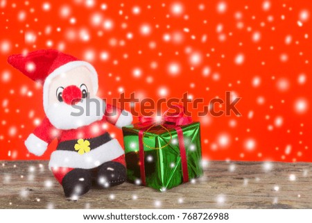 gift box and santa claus doll on the wooden table with snow and red background