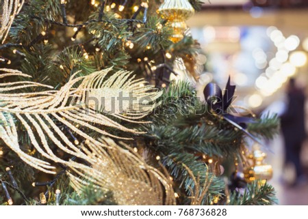 Christmas tree with golden balls and lights with copy space on blurred bokeh background in mall. Close up. Toned image. Abstract Xmas pattern. 