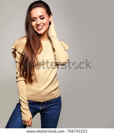 Portrait of beautiful smiling cute brunette woman model in casual beige warm sweater clothes with no makeup isolated on gray