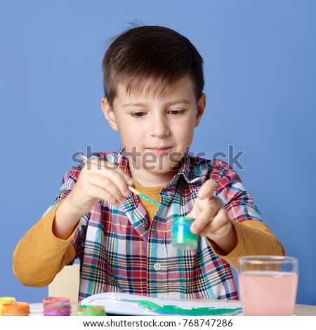 Smiling Caucasian boy is painting with watercolors.