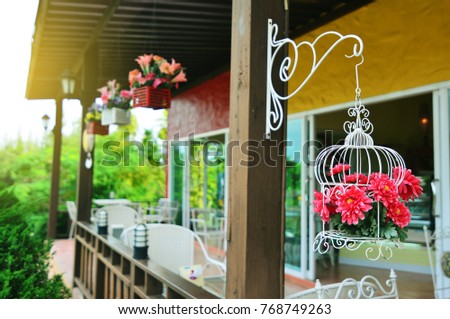 Red flower in the flowerpot made of steel wire shaped bird cage hanging on the balcony vintage house