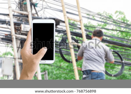 Man use mobile phone, blur image of technicians are installing an internet line as background.