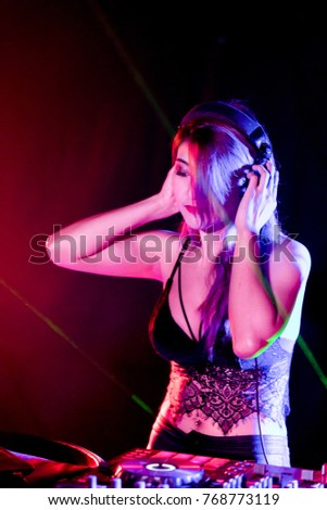 Blurred photo of DJ mixing music on colorful background. Beautiful DJ listening to the music in headphones, party concept. Selective focus blurred background. Dj mixes the track in the nightclub.
