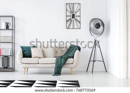 Green blanket on beige settee in bright living room with lamp and clock on white wall with copy space Royalty-Free Stock Photo #768773569