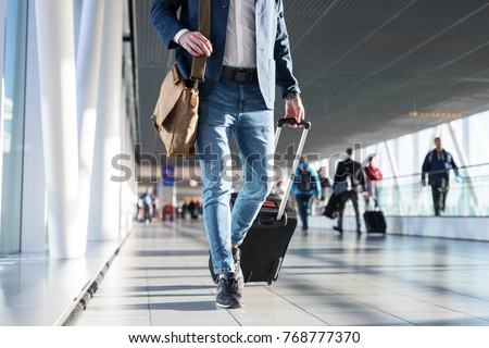 Man with shoulder bag and hand luggage walking in airport terminal Royalty-Free Stock Photo #768777370