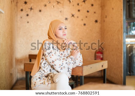 Beautiful Muslim Girl Fashion portraiture.Young Muslim Girl wearing Hijab,Casual Muslim Dress and Pant seating in the Hipster Cafe with wooden furniture.