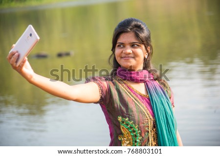 Happy young Indian girl taking a selfie on smartphone at outdoor. 