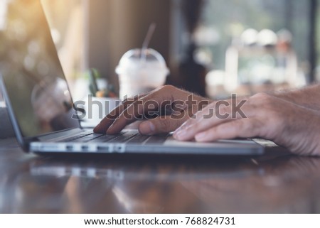 Casual business man or freelancer working on laptop computer with cup of coffee on table in cafe or coffee shop, anywhere office, online working concept, toned image