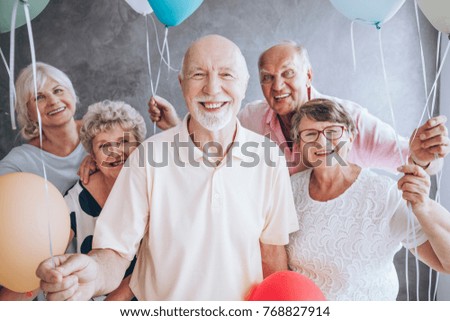 Smiling elderly man and his friends with balloons enjoying his birthday party