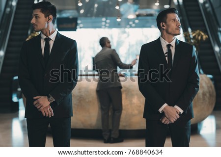 two bodyguards waiting for businessman standing at reception counter Royalty-Free Stock Photo #768840634