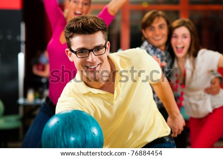 Group of four friends in a bowling alley having fun, three of them cheering the one in charge to throw the bowling ball