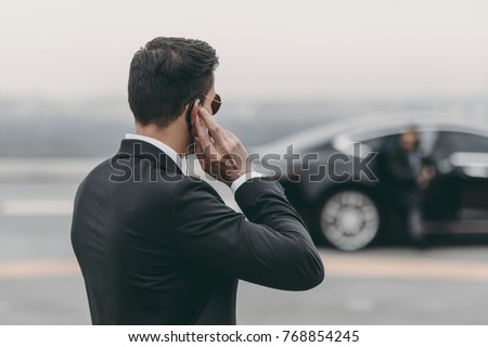 handsome bodyguard standing and listening message with security earpiece on helipad Royalty-Free Stock Photo #768854245