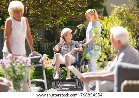 Senior woman in wheelchair spending time outside, getting some fresh air with her nurse from rest home Royalty-Free Stock Photo #768854554