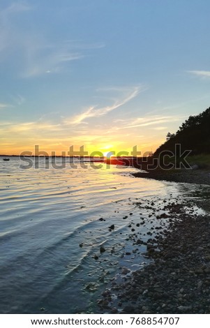 Portrait picture of the sun setting in the ocean on the horizon taken from a beach in Denmark