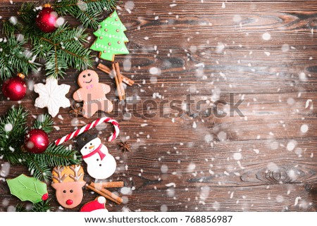Christmas gingerbread funny cookies with fir branches, cinnamon sticks, candy cane and decoration flat lay on wooden table, copy space. Christmas food composition, vintage toned image with snow effect