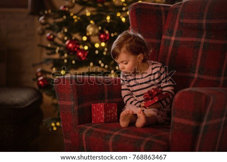little girl sitting in a red chair by christmas tree 