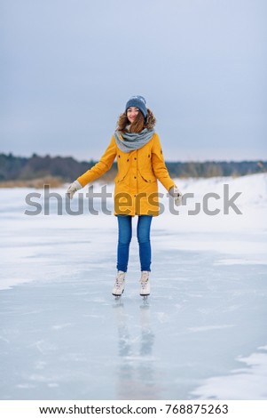 Young beautiful girl in yellow jacket is skating at winter on a frozen lake.
