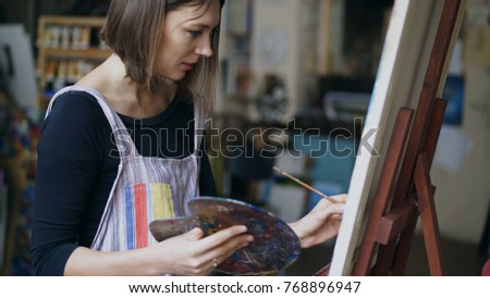 Young painter girl in apron painting still life picture on canvas in art-class