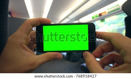 Hands holding (using) a smartphone with a green screen on the train. Close-up shot