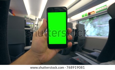 A hand holding (using) a smartphone with a green screen on the train. Close-up shot