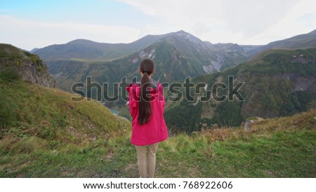 A young lady in red jacket in the mountains. Long shot.