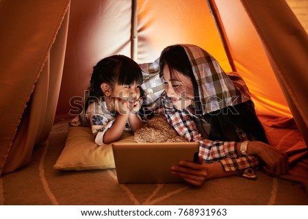Pretty mother and daughter watching cartoons on digital tablet