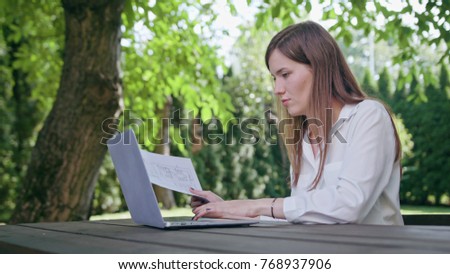 Business lady using a laptop entering data from paper. Medium shot. Soft Focus