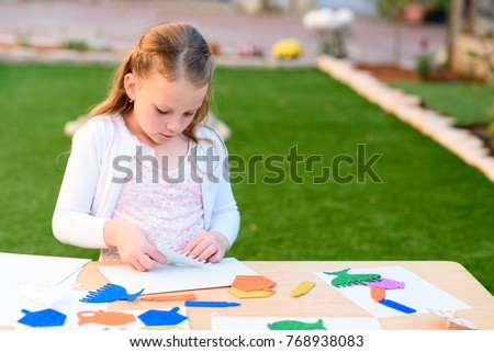 Little girl create a greeting card image of the Jewish holiday of Hanukkah.   Chanukkah decorations: sticking menorah,candles,dreidel, paper, leaves on wooden table. Needlework, crafts for children.