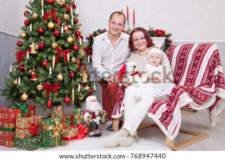 Christmas or New year celebration. Portrait of cheerful young family of three people near the Christmas tree with xmas gifts. A fireplace with christmas stocking on background. Happy holidays