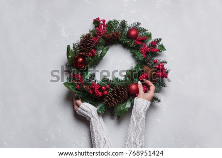 female hands holding Winter and christmas wreath with pine cones juniper fir and ivy leaves on gray background