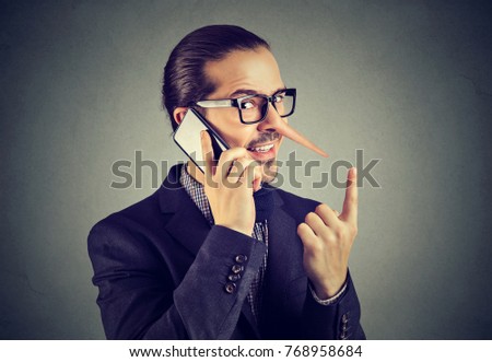 Sly liar business man with long nose talking on mobile phone isolated on gray wall background. Royalty-Free Stock Photo #768958684