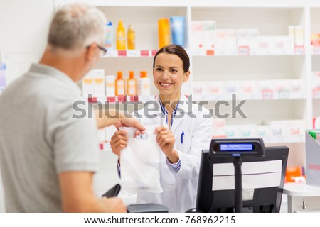 medicine, pharmaceutics, health care and people concept - female apothecary giving senior male customer his purchase in bag at drugstore Royalty-Free Stock Photo #768962215