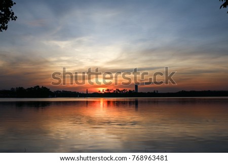 beautiful nature of sunset over the lake show refection on water with silhouette tree and building with blue and orange twilight sky
