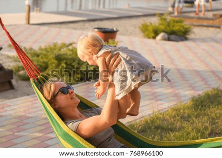 Young mother relaxing with daughter in hammock on the beach