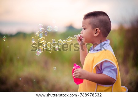Cute kid blowing bubbles outdoors, in the forest in a beautiful sunny afternoon