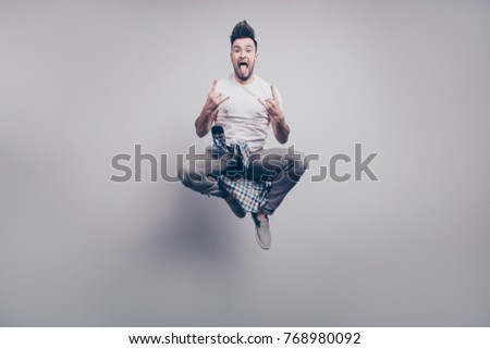 Happiness, freedom, motion and people concept. Crazy, bearded attractive handsome music lover jumping in air, gesturing rock and roll sign with hair up and tongue out over grey background