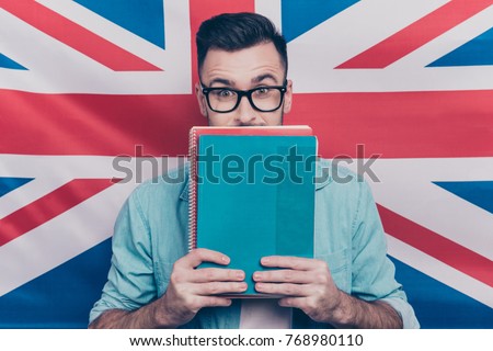 English language learning concept-portrait of excited man holding colorful copy books in hands closing half face with notebooks standing over English flag background Royalty-Free Stock Photo #768980110
