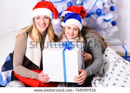 Christmas morning and New Year concept. Family or friends in Santa hats near present boxes. Sisters unpack big gift boxes. Girls with happy faces near white and blue Christmas tree on background.
