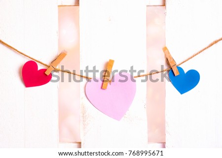 Valentine day theme image with one big pink heart in the middle, one red and one blue on the sides, made from paper and tied to a string with wooden clips.
