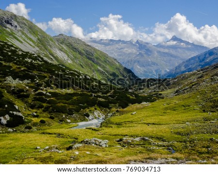an alpine landscape in the austrian alps, grassland with rocks and little trees and a small creek flowing through all downwards a narrow valley