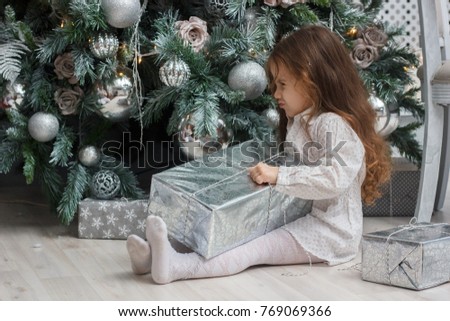 Little kid girl sitting near the christmas tree with the gift at hand.