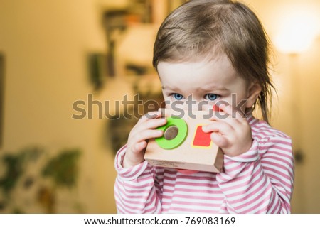 Toddler girl playing with her toy photo camera at home, wearing striped turtleneck sweater