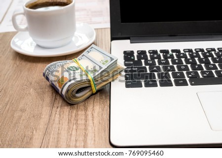 stack of dollar, cup of coffee and laptop on desk