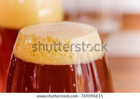 Close up of glass of dark beer with foam in a blurred background