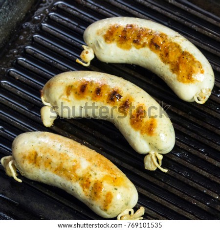 A square picture. Grilled sausages for grilling in a black frying pan. Close-up.