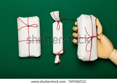 Hand holding a Christmas present, composition with small simple wrapped presents on green background. Giving a gift