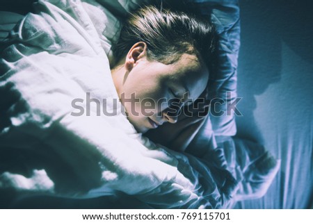 Pretty young brunette woman sleeping in huge bed with lamp on (color toned image)