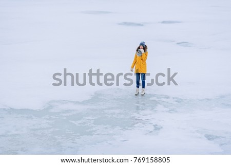 Young beautiful girl in yellow jacket is skating at winter on a frozen lake. Top view.