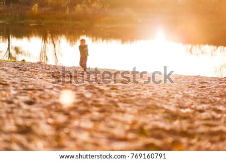 A happy boy having fun in the park in autumn walking and running near the water. Family, love, happiness concept. A picture filled with sunset  light
